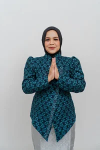 Seorang wanita berpakaian seragam biru dan putih, dengan tangan bersamaan di depan tubuhnya, berdiri dengan mata tertutup.