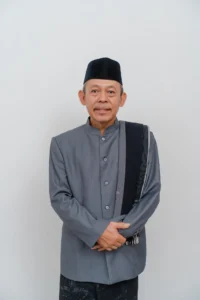 Seorang pria dalam pakaian formal berdiri dengan tangan terkait di depan tubuhnya.