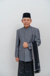 Seorang mantan kepala Kementerian Pendidikan dan Kebudayaan Provinsi Purbalingga berdiri dalam pakaian formal dengan tangan terbuka.