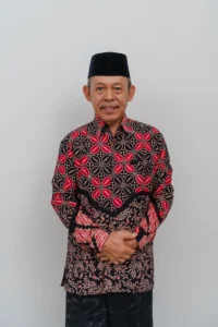 Seorang pria dalam pakaian tradisional Indonesia berdiri dengan tangan terbuka di depan dirinya.