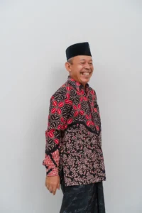 Seorang pemimpin kementerian dalam pakaian tradisional, tersenyum dan berpose untuk kamera.