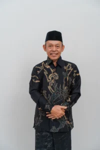 Seorang pria dalam pakaian tradisional berdiri dengan tangan terbuka di depan dirinya.