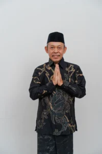Seorang pemimpin kepala Kementerian Kebudayaan dan Pariwisata Provinsi Purbalingga berdiri dengan tangan bersama di depannya, memakai pakaian polos berwarna biru gelap dan emas, dan