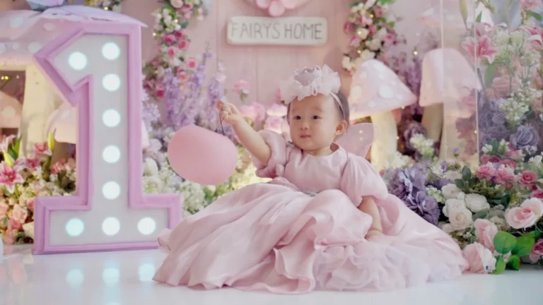 Bayi berpakaian seperti putri pernik, bermain dengan balon di depan dekorasi tema pernik.